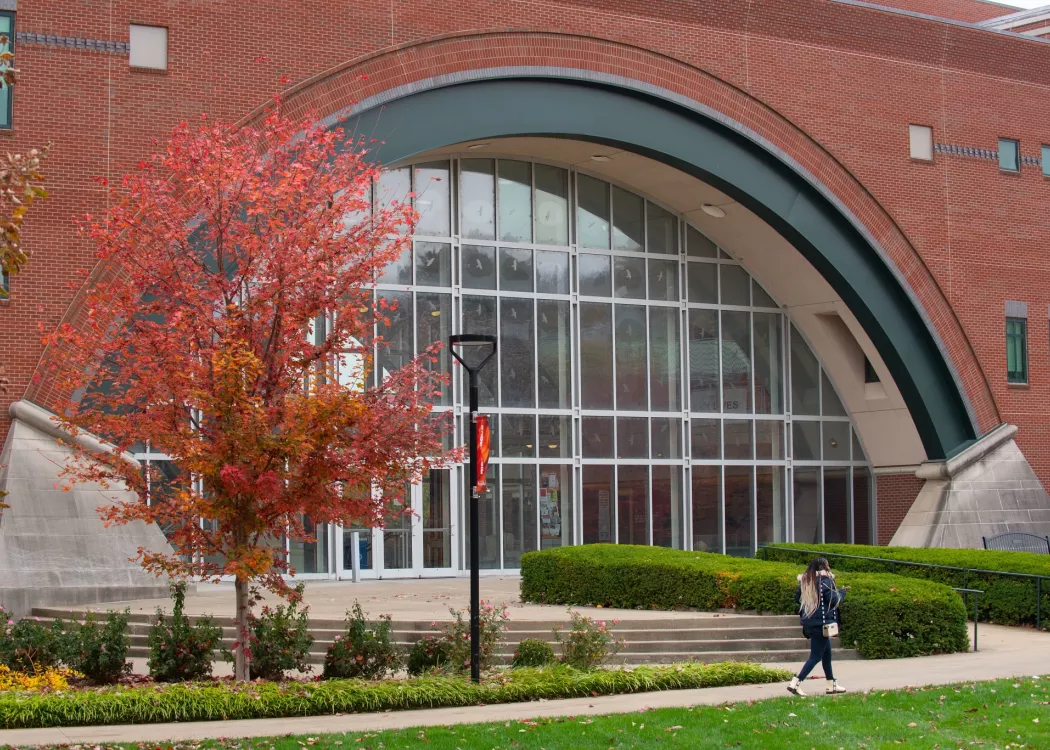 Front view of large rounded window of Lutz Hall entrance on a fall day. Female walking along sidewalk.