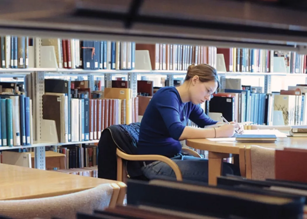 Student sitting at a table and reading in a library.